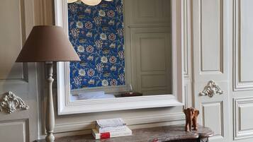 Een kamer met een grote spiegel, een lamp, een open haard en behang met een patroon.