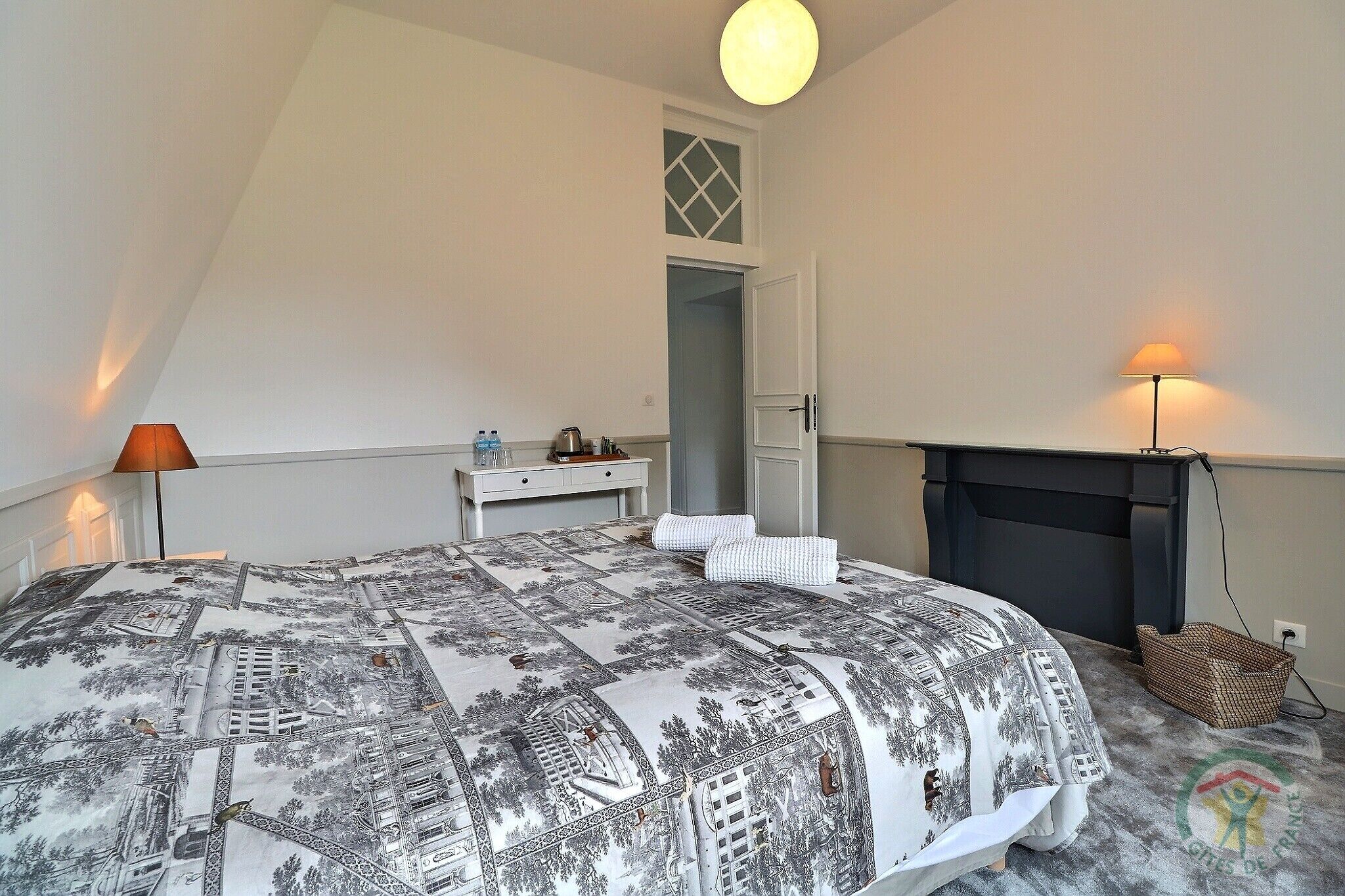 A bedroom with a bed, bedside table, lamp, and a fireplace.