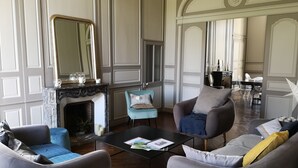 A spacious living room with a fireplace, two armchairs, a coffee table, and a dining area in the background. - Domaine des Longrais (Saint-Thurial)