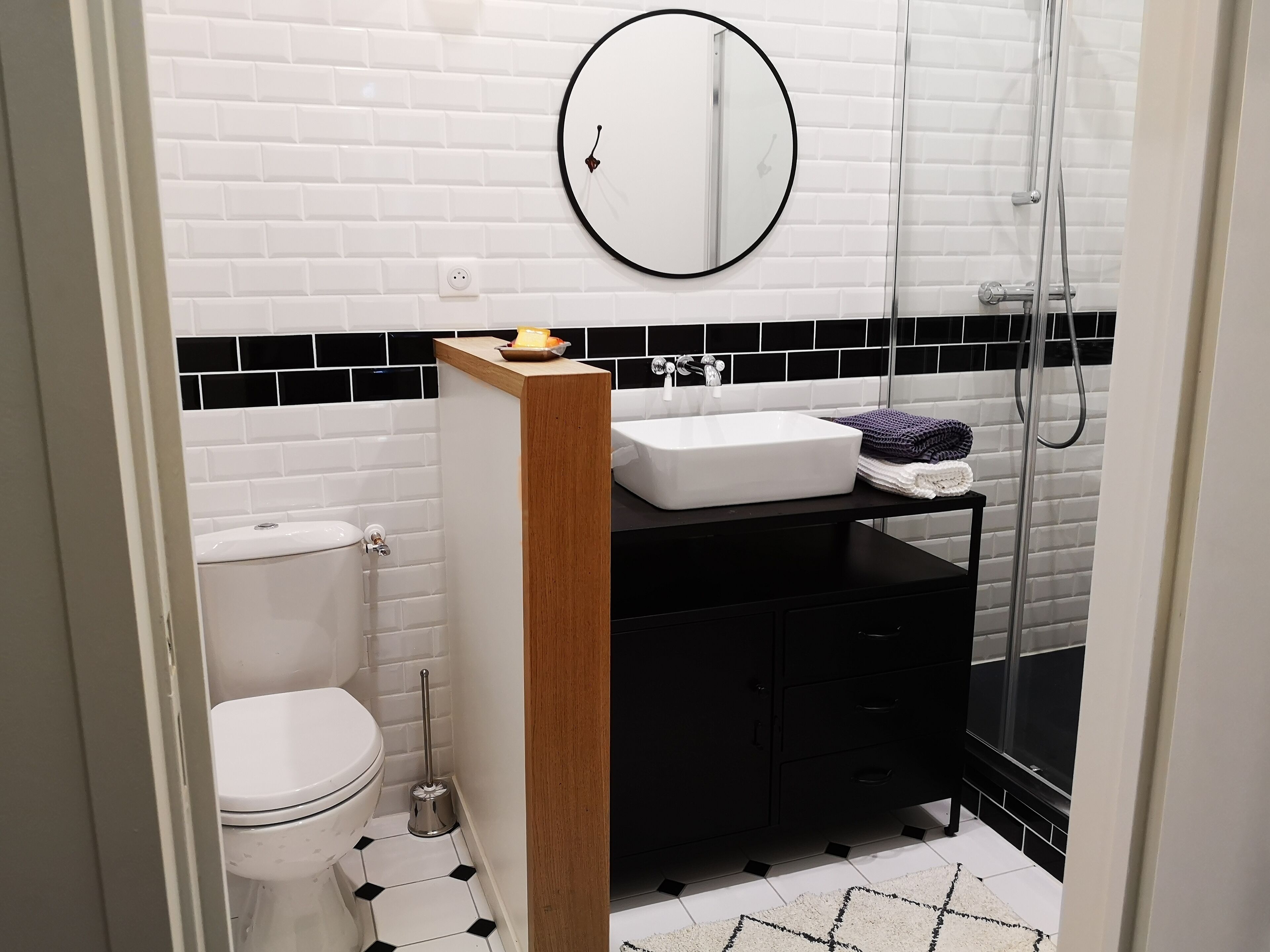 Un baño moderno con inodoro blanco, lavamanos negro y espejo superior, además de una zona de ducha.