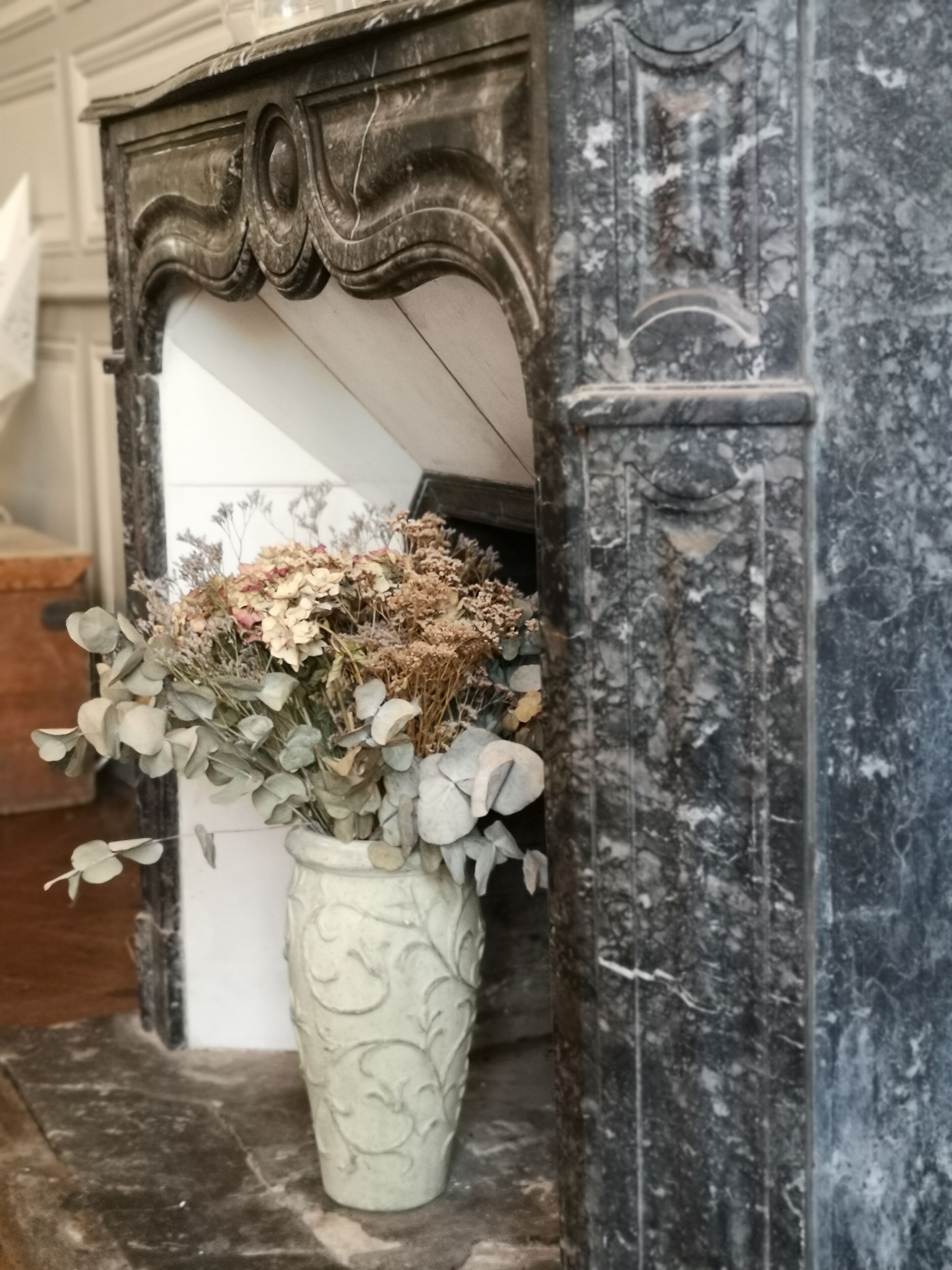 Un jarrón blanco con un arreglo floral sobre una superficie de mármol.