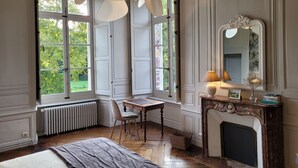 A room with large windows, a fireplace, a table, and a chair. - Domaine des Longrais (Saint-Thurial)