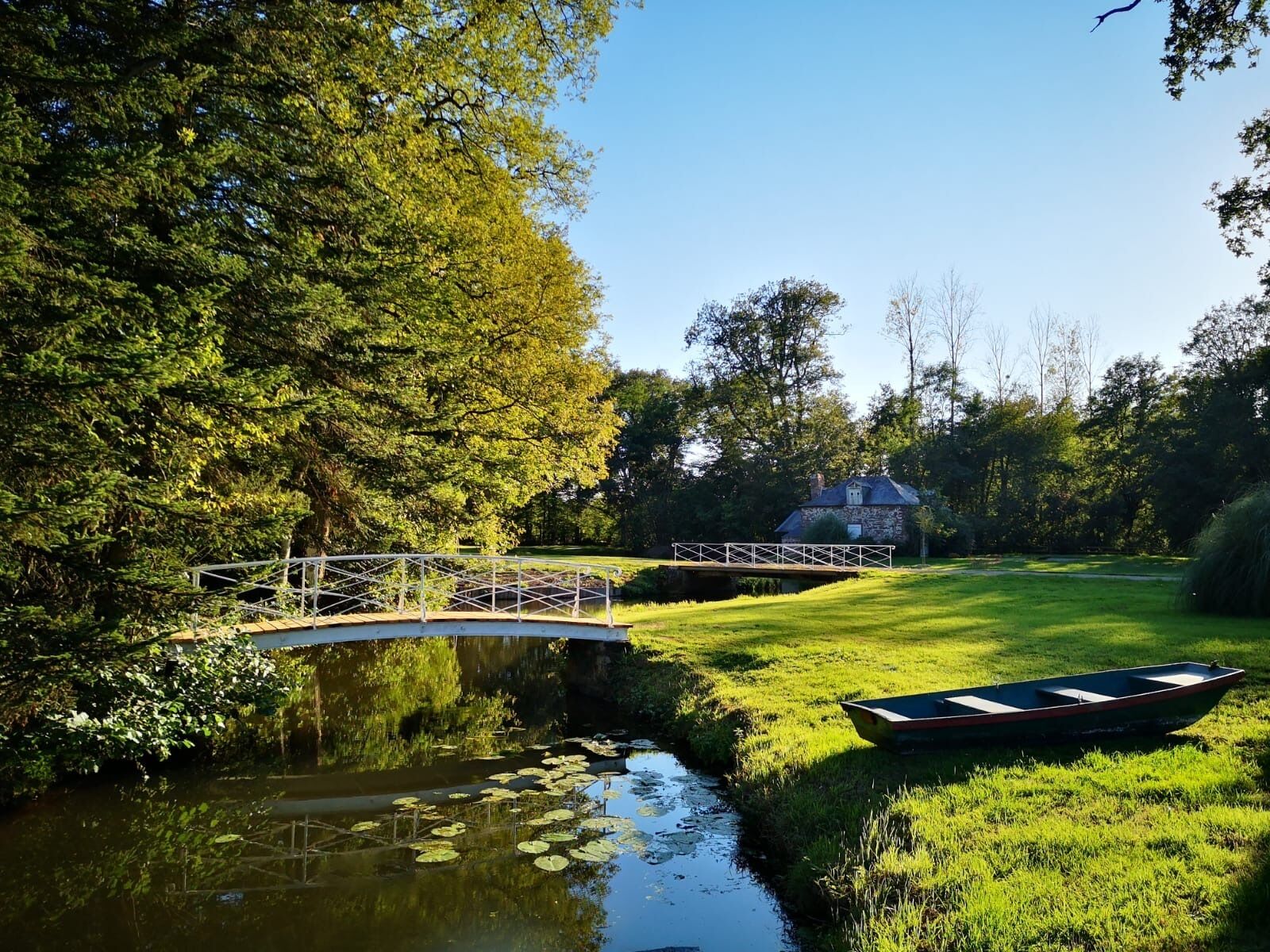 A serene riverside scene with a small bridge, a stone building, and a rowboat.