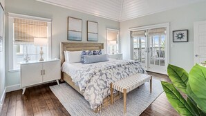 Quarto com cama, mesas de cabeceira, um banco e uma janela grande.