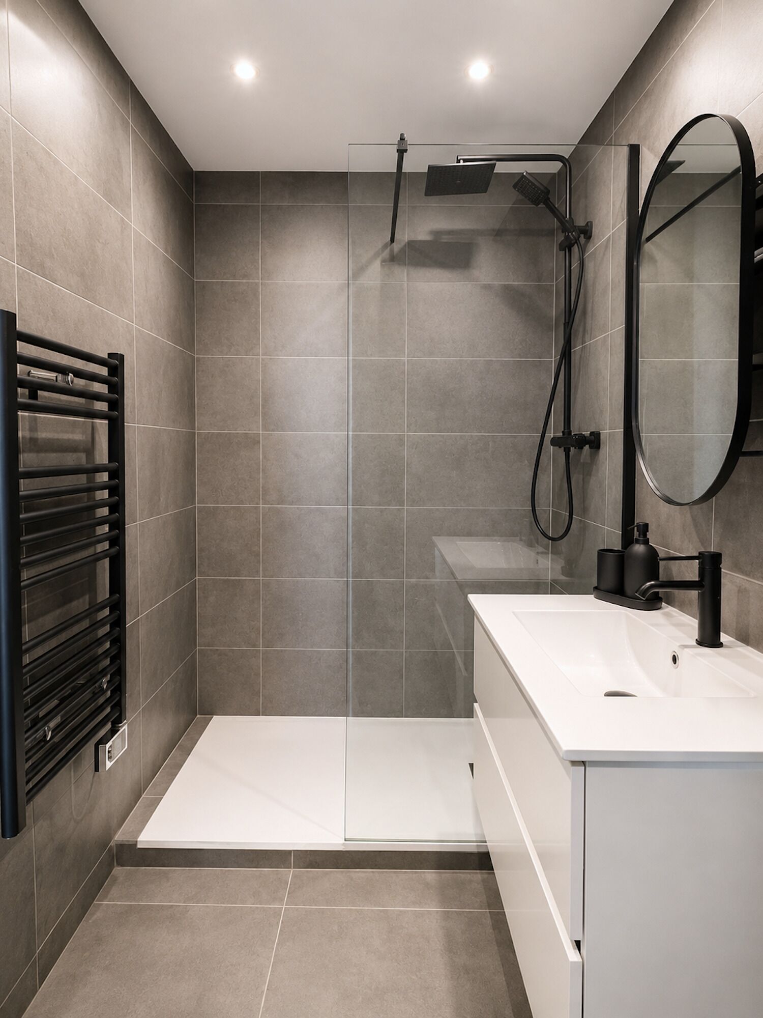Een moderne badkamer met een douchecabine van glas, een witte wastafel en een zwarte handdoekhouder.