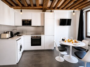 Une cuisine moderne avec des meubles blancs, un four encastré, un lave-linge et un coin repas comprenant une table et des chaises.