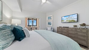 A spacious bedroom with a large bed, a dresser, a television, and artwork on the wall.