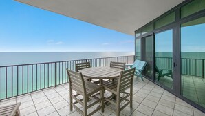 Un balcon avec une table et des chaises, une porte vitrée et une vue sur la mer.