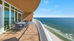 A balcony with a wooden deck, a table with chairs, and a view of the ocean.