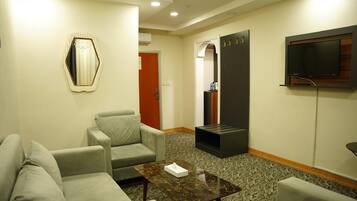 A hotel room with a sofa, a coffee table, a TV mounted on the wall, and a small black cabinet.