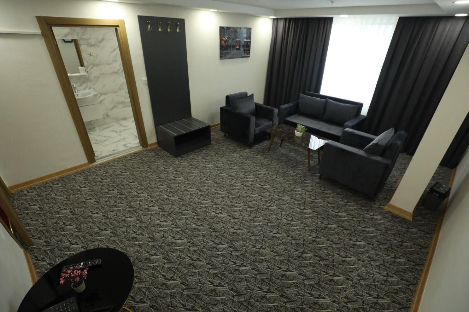 Una habitación con alfombra estampada, un sofá, una mesita con una planta, un espejo y una puerta con perchero.