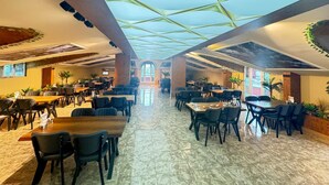 Un restaurant spacieux avec un plafond haut et un décor géométrique en verre. Les tables et les chaises sont disposées de part et d’autre d’une allée centrale.
