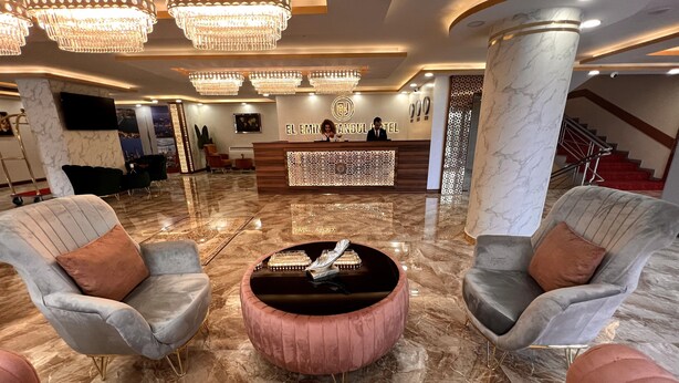 Un hall d’hôtel avec un sol en marbre, un comptoir d’accueil et deux fauteuils avec des coussins.