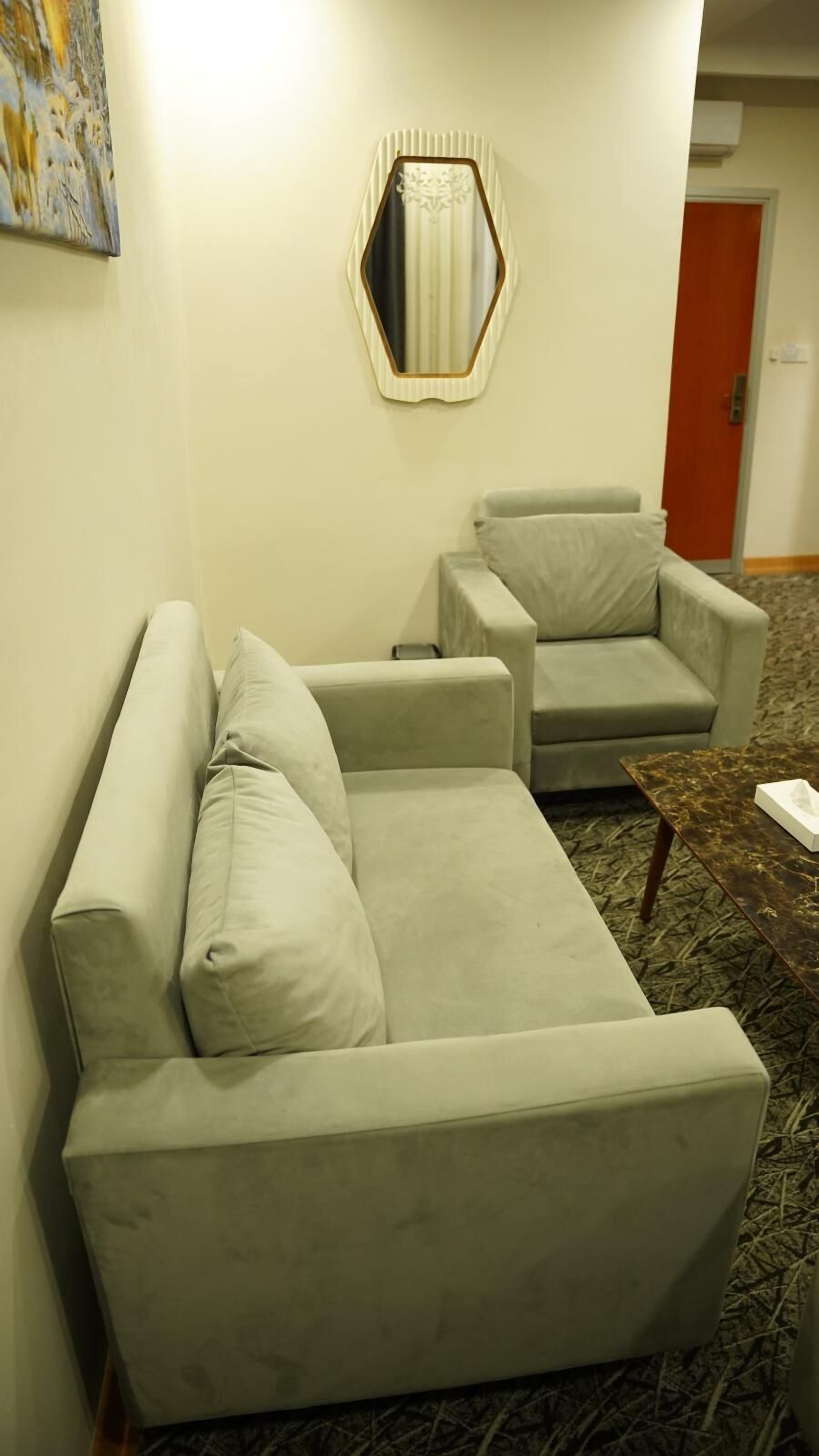 A room with a light-colored sofa and armchair, a small table, and a decorative mirror on the wall.