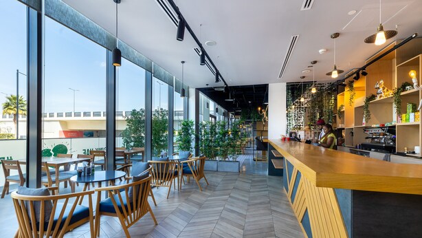 A modern cafe with large windows, wooden chairs, and a bar area. - INK Hotel (Dubai)