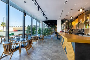 A modern cafe with large windows, wooden chairs, and a bar area. - INK Hotel (Dubai)