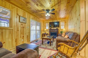 L’intérieur d’un chalet en bois, avec une cheminée, un canapé en cuir et un ventilateur de plafond.