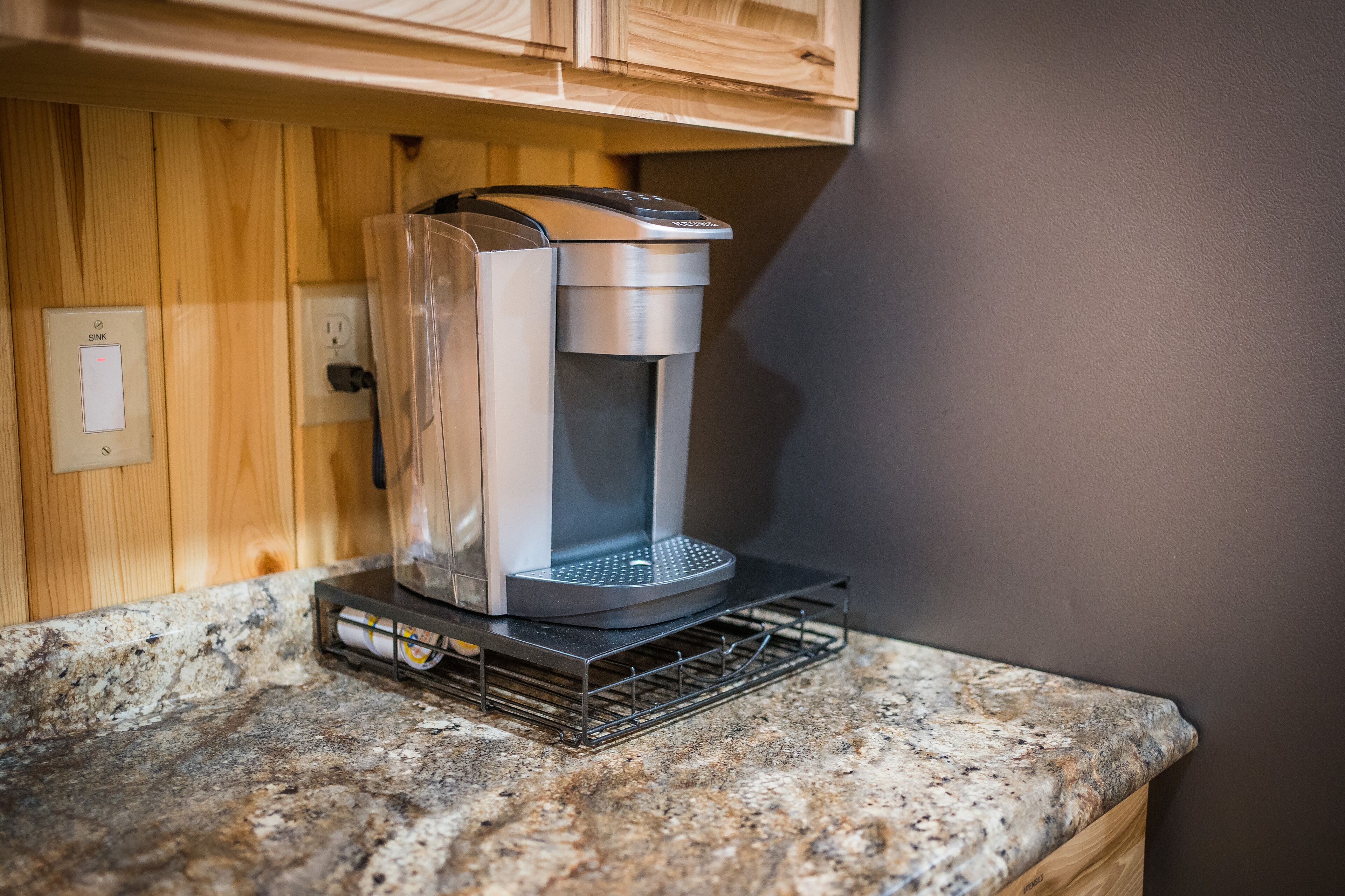 Una cafetera sobre una encimera de granito con un mueble de madera encima.