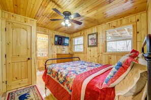Une chambre dans un chalet en bois, avec un lit, un ventilateur de plafond, une télévision et une fenêtre.