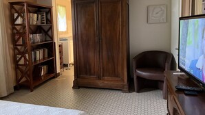 Une chambre d’hôtel avec une grande armoire en bois, une bibliothèque, un fauteuil en cuir et un téléviseur.