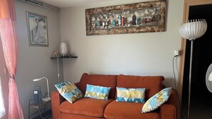 Un salon comprenant un canapé, des coussins à motifs, une table basse aux formes géométriques, un lampadaire et une œuvre d’art murale.