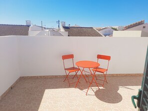 A small outdoor patio with a table and two chairs, a tiled floor, and a view of neighboring buildings.