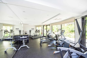 Ein Fitnessstudio mit verschiedenen Trainingsgeräten, großen Fenstern und einem schwarzen Boden.