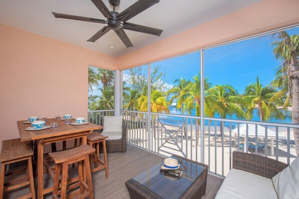 A balcony with a view of a pool and palm trees, wooden furniture, and a ceiling fan.