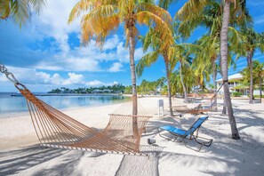 A beach with a hammock, lounge chairs, and palm trees.