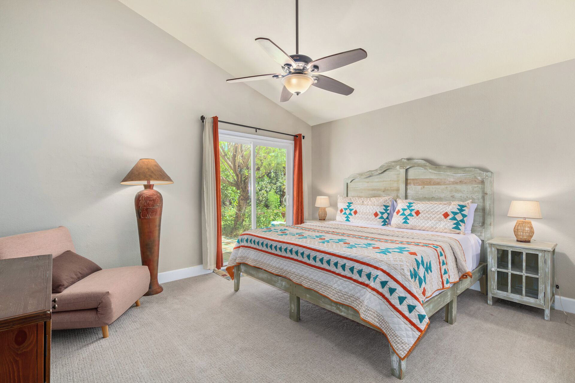 A bedroom with a bed, a chair, a nightstand, a lamp, and a ceiling fan.