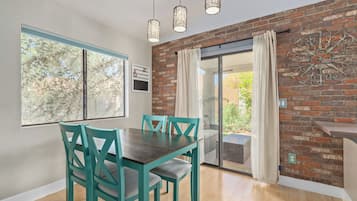 A dining area with a wooden table and teal chairs, a brick wall, and a sliding glass door leading to an outdoor patio.