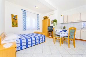 A compact room with a bed, a small table with chairs, a television, and a kitchenette. - Apartments Mario (Novalja)
