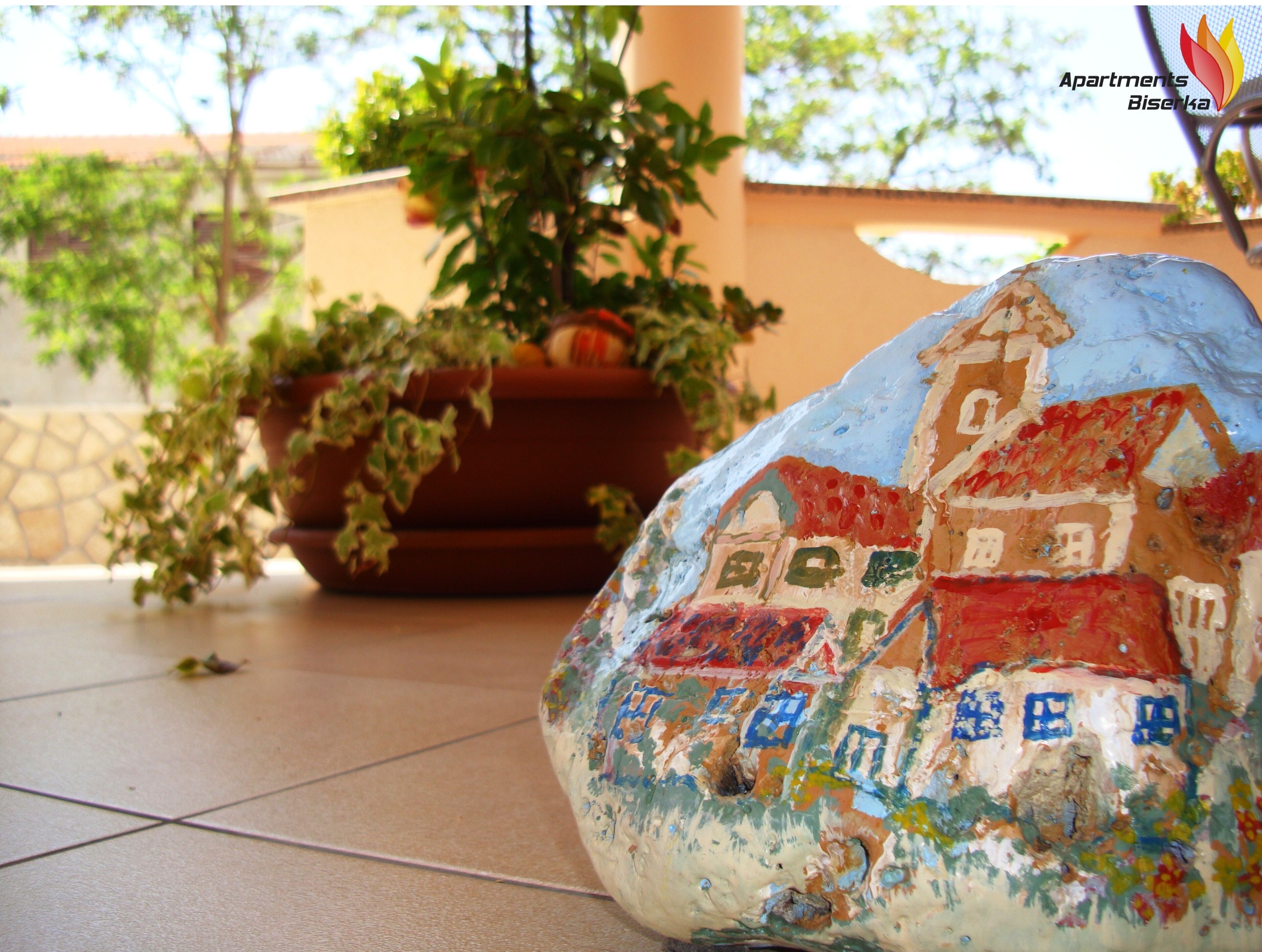A rock with a painted house, a potted plant, and a tiled floor.