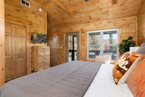 Un dormitorio de cabaña de madera con una cama, un televisor, una puerta y una ventana.