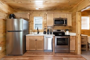 Una cocina compacta con paredes de madera, un refrigerador de acero inoxidable, un microondas, un lavavajillas y un horno.