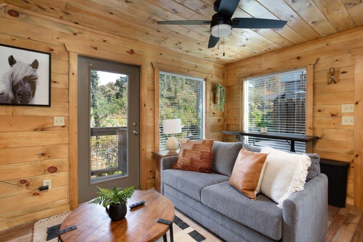 A wooden cabin interior with a sofa, a table, and a ceiling fan.