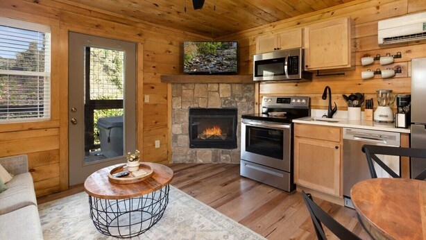 Un interior de cabaña acogedor, con chimenea de piedra, techo de madera y electrodomésticos de cocina modernos.