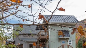 Una casa rústica con cimientos de piedra, una terraza de madera y un pequeño arroyo en primer plano.