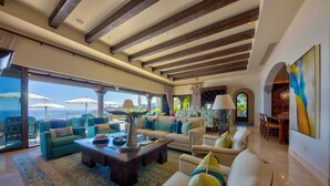 Uma sala de estar ampla com uma grande janela com vista para o mar, mobiliada com sofás e uma mesa de centro.