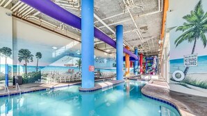 An indoor swimming pool with a mural of a beach scene, lounge chairs, and a sign indicating shallow water with no diving allowed. - 🐠Oceanfront | Indoor Heated Water Park + Lazy River | Dunes Village Resort 701 (Myrtle Beach)