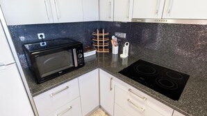 Une cuisine moderne avec des armoires blanches, un micro-ondes noir, une cuisinière encastrée et un porte-épices.