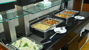 A buffet setup with various food items in trays, a glass display case, and a tissue box.