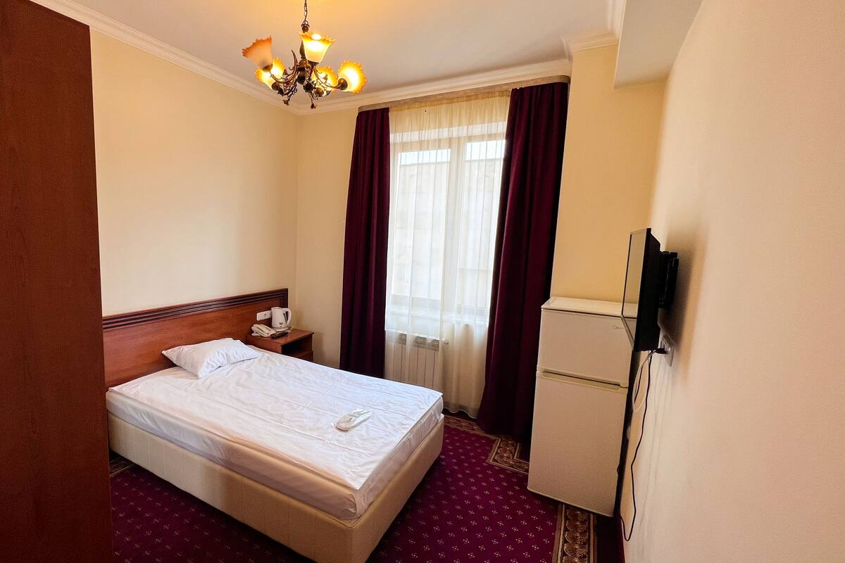 A hotel room with a bed, a nightstand, a television, and a window with curtains.