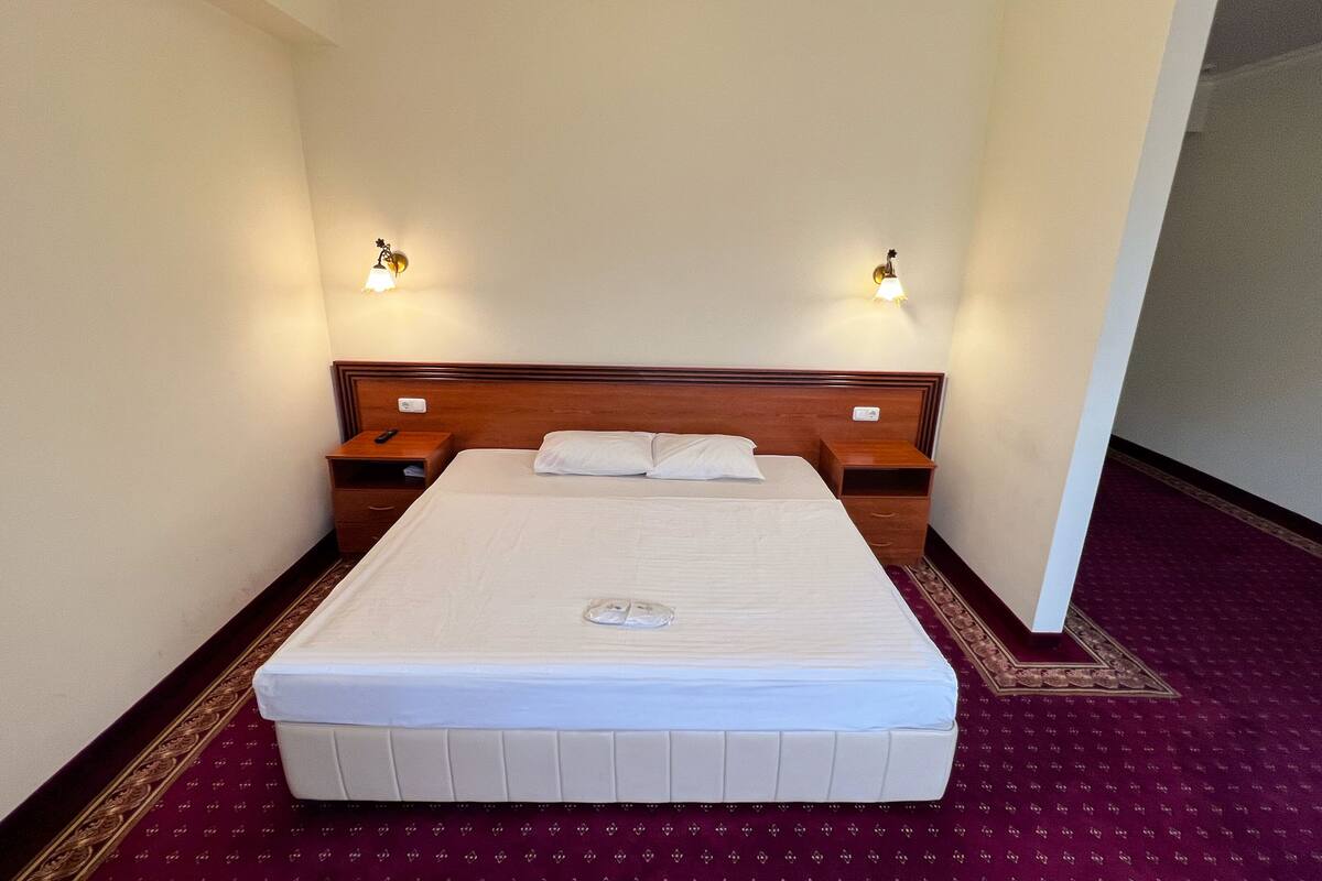 A hotel room with a large bed, two bedside tables, and two wall-mounted lamps.
