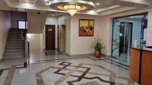 A hotel lobby with a staircase, a reception desk, a large abstract painting, and a potted plant.