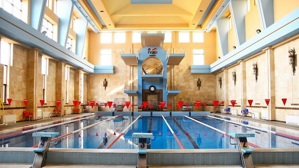 A large indoor swimming pool with multiple lanes, a central archway, and a high ceiling with skylights.