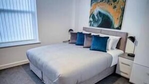 A modern bedroom with a large bed, a painting on the wall, and a window with blinds. - One Bed Serviced Apartment Preston (Preston)