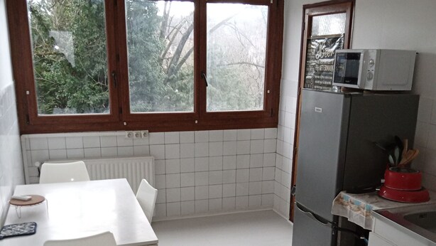 Een kleine keuken met een witte tafel, stoelen, een koelkast en een magnetron.