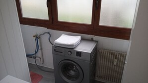 Een kleine wasruimte met een voorlader wasmachine, een radiator en een raam boven de machine.