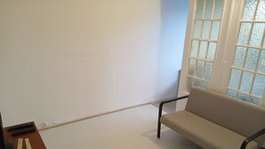 Een kamer met een beige bank, een houten bijzettafeltje en een raam met geblakerd glas.